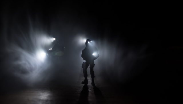 Anti-riot police give signal to be ready. Government power concept. Spec ops police in action. Smoke on a dark background with lights. Blue red flashing sirens. Selective focus